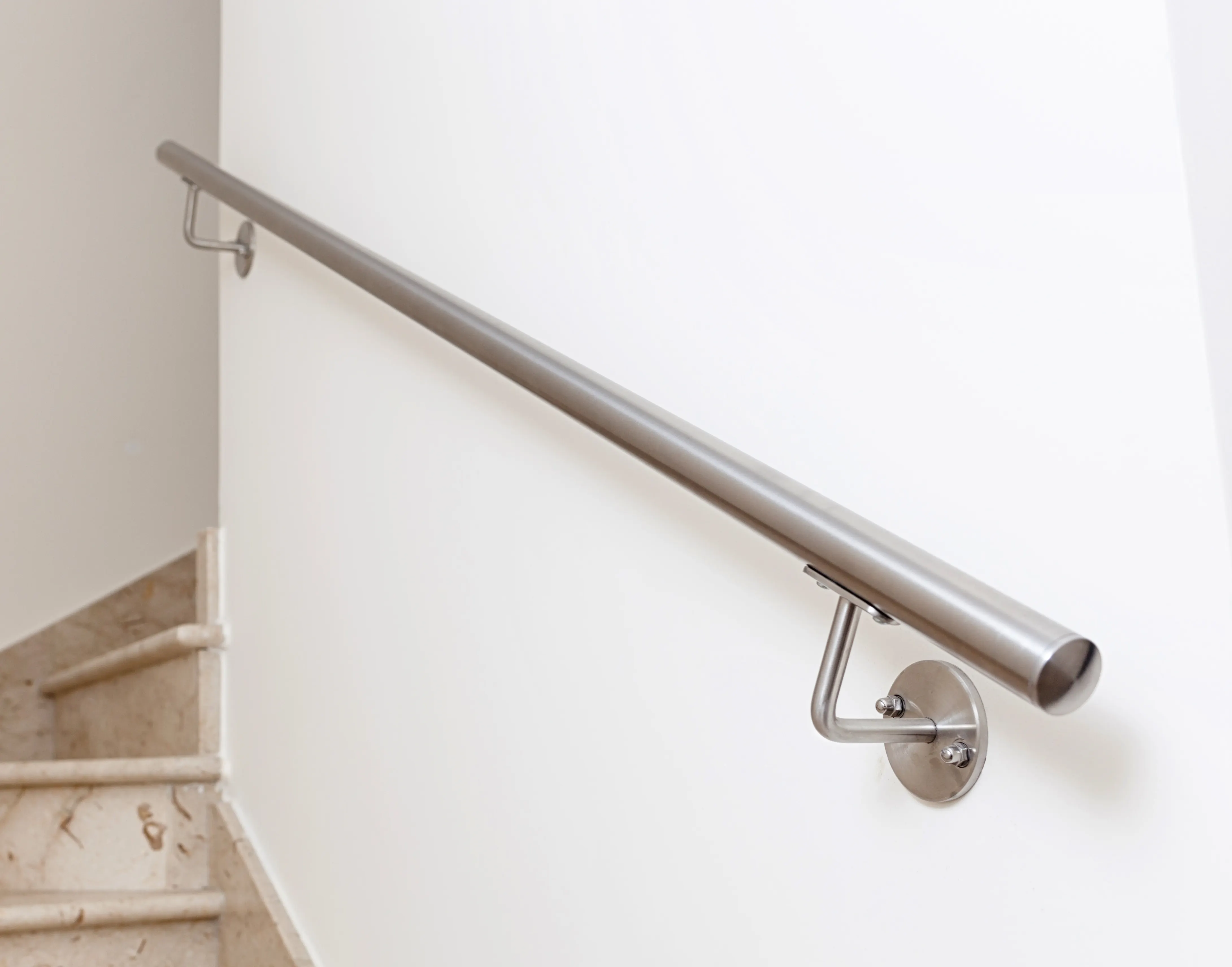 A satin steel handrail running along a calm white wall above a staircase